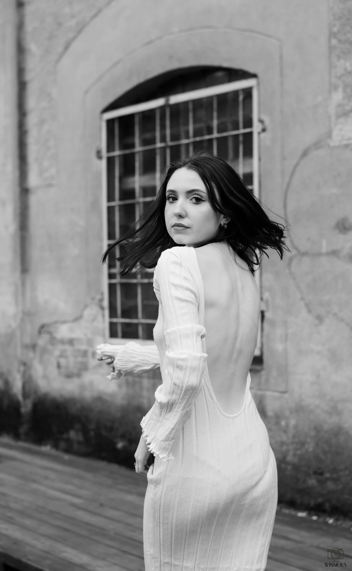 Czarno-biały portret kobiety w jasnej sukni na tle starego budynku